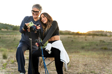 Senior and young women using smartphone during nordic walking