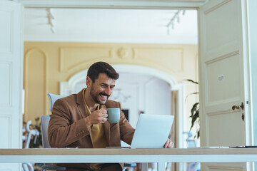 Smiling Business Professional Working on Laptop at Bright Office Desk Drinking Coffee During Morning Session