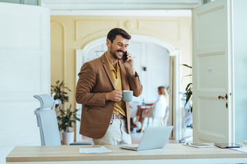 Smiling Businessman On Phone With Coffee In Modern Office At Desk