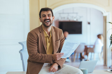 Confident Businessman Laughing While Holding Documents in Modern Office During Meeting Break