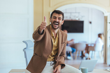Confident Man Gives Thumbs Up In Modern Office Café, Celebrating Success With Colleagues During Break