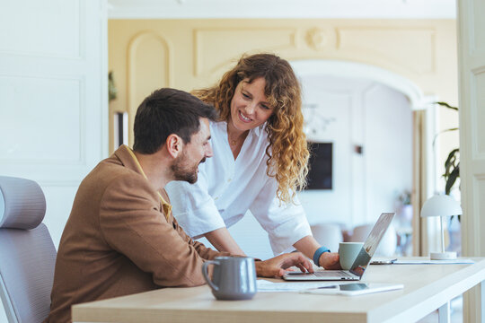 Friendly Office Collaboration Between Colleagues Over Laptop At Modern Open-Plan Desk