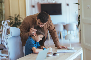 Father Helps Son With Homework At Modern Desk In Bright Home Office Setting