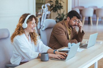 Happy Team At Work: Woman Laughing With Headphones While Man Focuses On Laptop In Modern Open Office