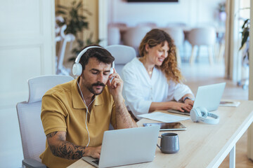 Focused Teamwork At Modern Co-Working Desk With Laptops And Headphones In Office