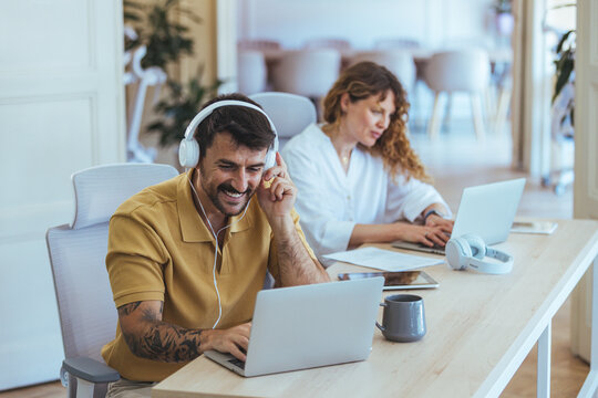 Focused Team Working at Shared Desk With Laptops and Headphones in Modern Office
