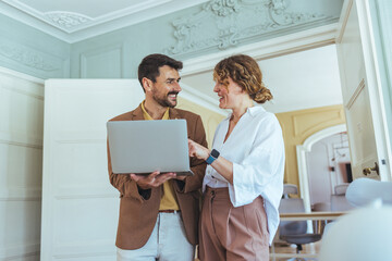 Two Colleagues Share Laptop in Bright Office, Discussing Project Ideas and Collaboration