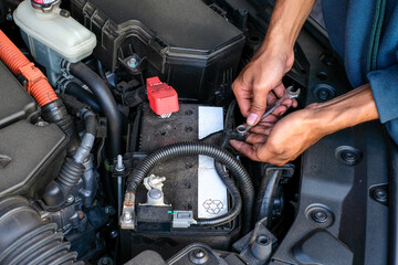 A mechanic replacing a car battery, tightening the terminal connection inside the engine bay. Perfect for vehicle maintenance, repair tutorials, automotive service, and battery replacement guides
