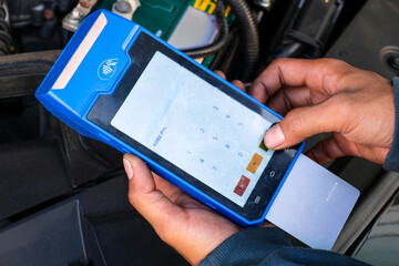 A mechanic holding a blue EDC machine to process a digital payment after vehicle maintenance. Perfect for advertisements, fintech promotions, garage service, and digital payment.