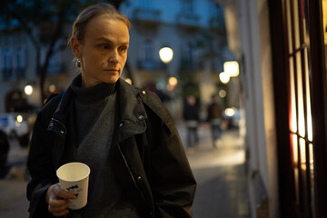 Woman with coffee cup in urban evening scene