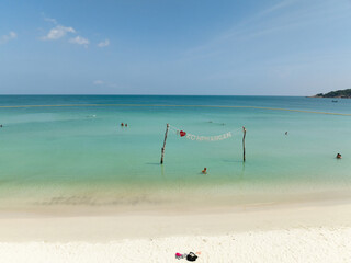 Wooden poles with Koh Phangan sign in turquoise sea near white sandy beach, under a bright sunny sky. Ko Pha Ngan, Thailand.