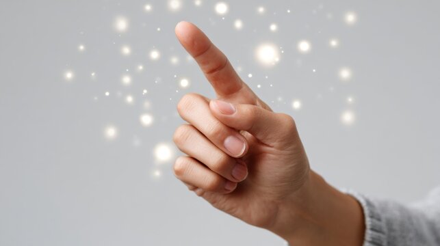 A close-up of a hand pointing upwards, surrounded by a magical glow of sparkling lights against a grey background.