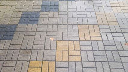 Close-up view of textured pavement with various colored tiles, including gray, blue, and yellow. Unique patterns create an interesting urban background for various uses.