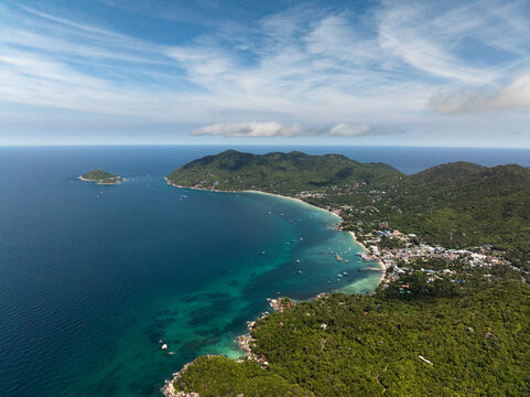 Aerial view of coastal hills covered in lush greenery with turquoise water and small islands dotting the ocean under a blue sky. Koh Tao, Thailand.