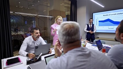 Businesswoman in a pink suit presents important data and analysis to her attentive coworkers during a corporate meeting. They are collaborating and discussing market trends in a modern office. - Powered by Adobe