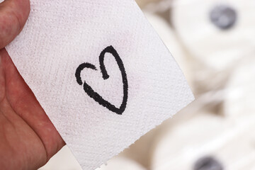 A hand holds a piece of white paper with a drawn heart symbol. The scene emphasizes affection through simple expression using toilet paper, ideal for emotional messages.