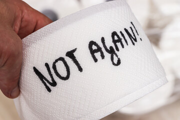 A hand holding a roll of toilet paper featuring handwritten text that says NOT AGAIN. The paper highlights a moment of exasperation or humor in everyday life.
