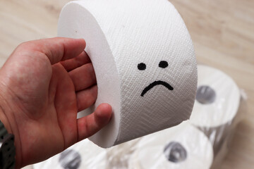 A hand holding a roll of toilet paper featuring a sad face. The context suggests humor in everyday life. Ideal for topics related to hygiene, emotions, or home supplies.