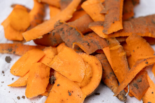 Close-up of orange carrot peels scattered on a white surface, highlighting their texture and color. Ideal for food-related projects and healthy cooking themes.