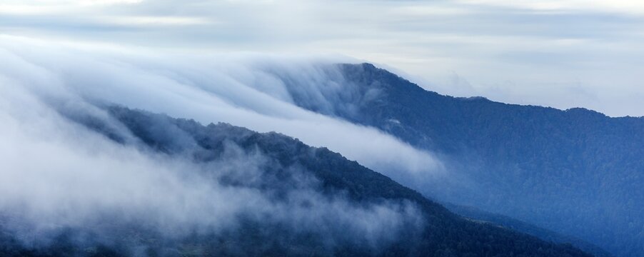 clouds spilling over the mountain ridge blue colored
