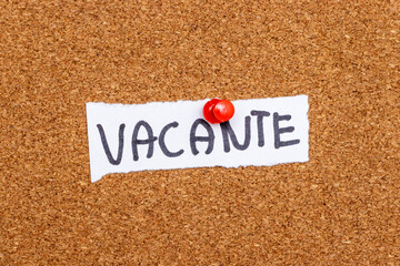 A handwritten note saying VACANTE pinned to a corkboard, symbolizing vacancy or availability in various contexts like job postings or real estate.