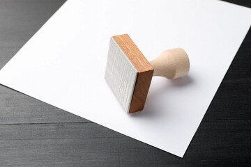 One wooden stamp and blank sheet of paper on black table, closeup. Space for text