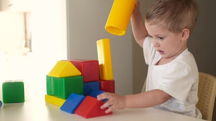 baby boy playing with toy a blocks in kindergarten. happy family kid dream education concept. blond child builds a house lifestyle from toy cubes on the table in kindergarten
