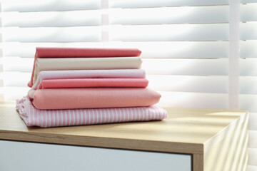 Stack of clean clothes on cabinet near window indoors, closeup