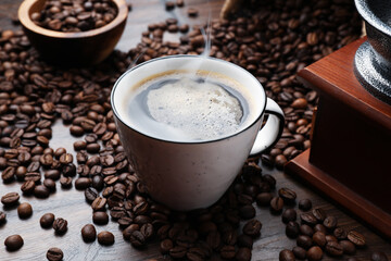 Aromatic coffee in cup, beans and grinder on wooden table, closeup