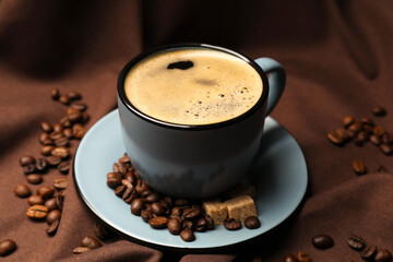 Aromatic coffee in cup, beans and brown sugar on fabric, closeup