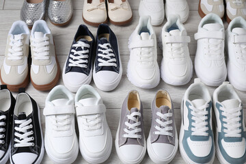 Many stylish kid's shoes on grey wooden floor, above view