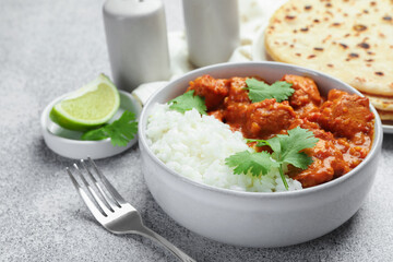 Delicious chicken tikka masala with rice, cilantro and fork on grey textured table, closeup