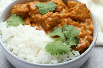 Delicious chicken tikka masala with rice and cilantro in bowl on grey textured table, closeup