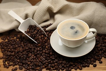 Aromatic coffee in cup and beans on wooden table, closeup