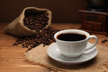 Aromatic coffee in cup, beans and grinder on wooden table, closeup