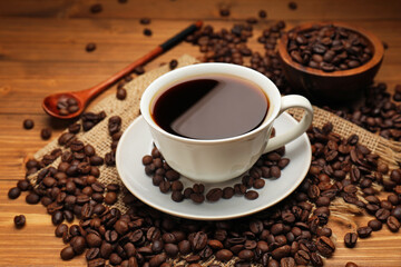 Fototapeta premium Aromatic coffee in cup and beans on wooden table, closeup