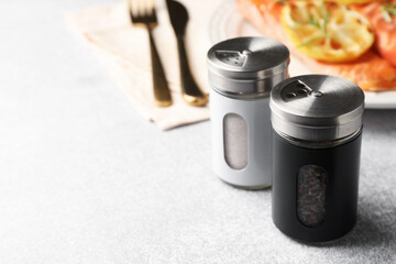 Salt pepper shakers and grilled salmon served on light table, closeup. Space for text