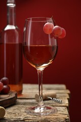 Rose wine in glass, bottle, grapes and corkscrew on wooden table against red background, closeup