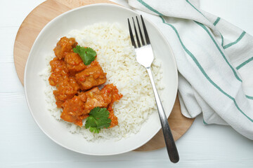 Delicious chicken tikka masala with rice, cilantro and fork on white wooden table, flat lay