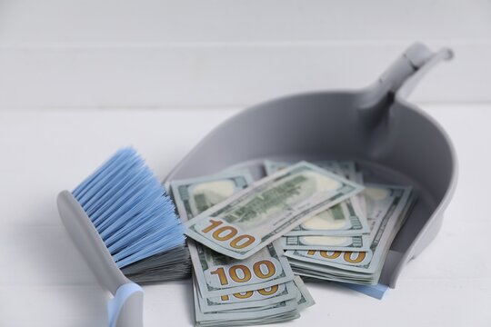 Dustpan with broom and dollar banknotes on white background, closeup. Space for text
