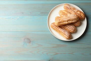 Tasty eclairs with powdered sugar on turquoise wooden table, top view. Space for text