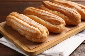 Tasty eclairs with powdered sugar on wooden table, closeup