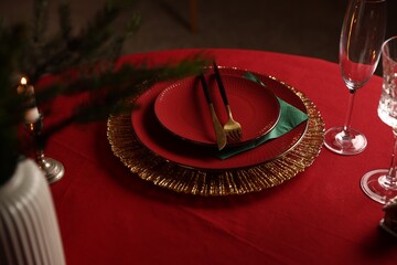 Christmas table setting with plates, glasses and burning candle in room, closeup