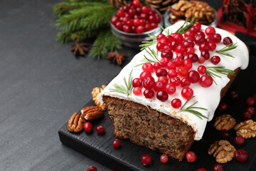Tasty Christmas cake with icing, cranberries, nuts, spices and festive decor on black table, closeup. Space for text