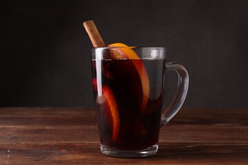 Tasty mulled wine with spices in glass cup on wooden table against dark background, closeup