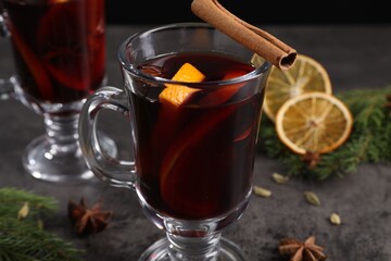 Tasty mulled wine in glass mugs, spices and fir branches on grey table, closeup