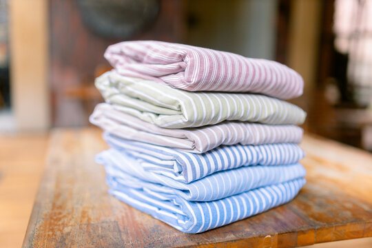 Freshly folded striped shirts stacked neatly on rustic wooden table, perfect for showcasing quality textiles, laundry services, or modern home organization solutions now