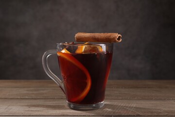 Tasty mulled wine with spices in glass cup on wooden table against gray background