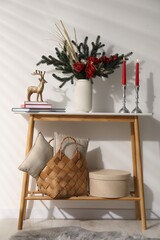 Different Christmas decor on console table near white wall indoors
