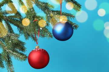Christmas balls hanging on fir tree branches against light blue background with blurred lights, closeup with space for text. Bokeh effect